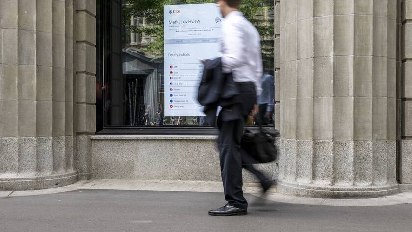Auf einem Bildschirm im Fenster der UBS Filiale an der Zürcher Bahnhofstrasse werden Börsendaten angezeigt. Ein Mann in weissem Hemd geht daran vorbei.
